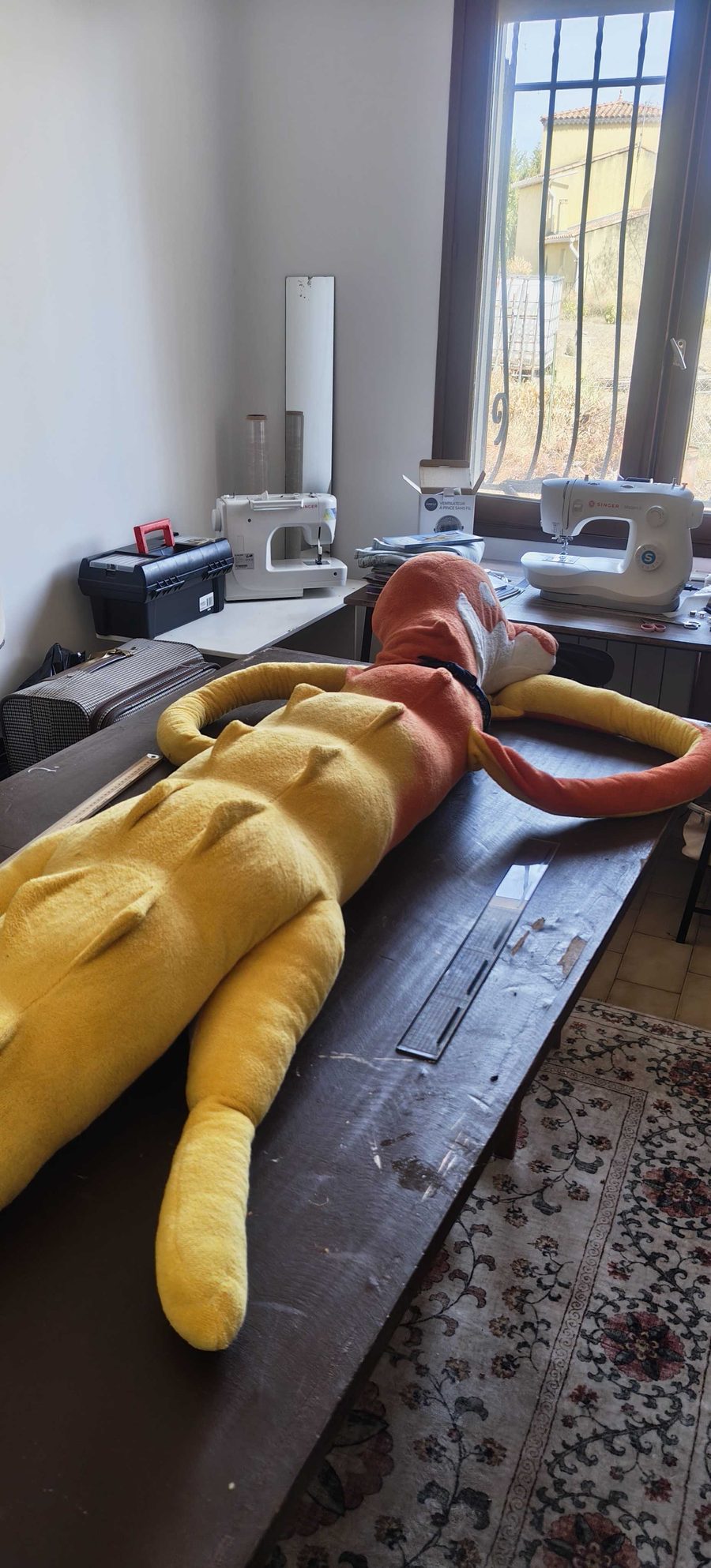 L'atelier de Kim Cuddle : deux machines à coudre près d'une fenêtre ensoleillée et un crocodile géant en cours